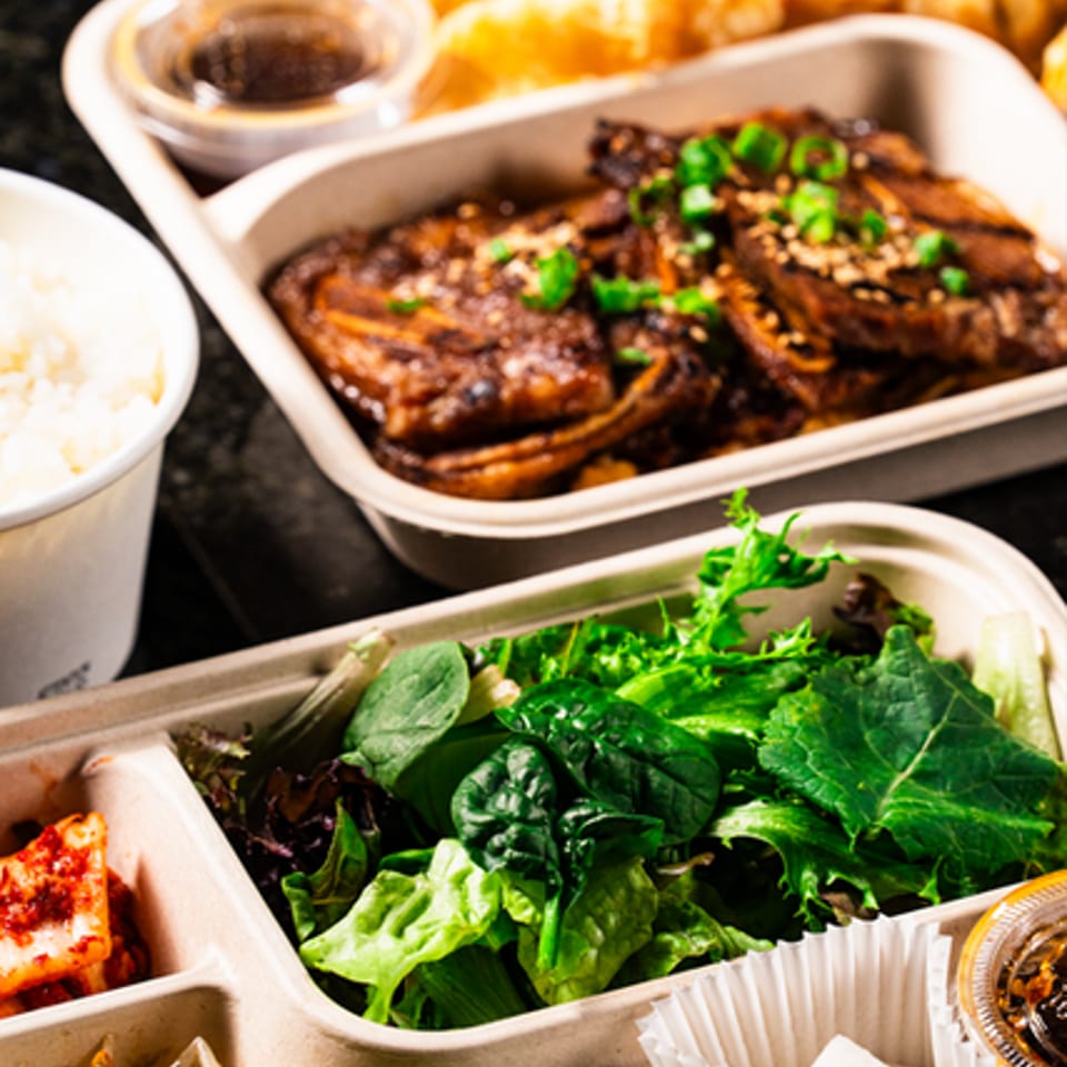 Korean-style meal with grilled meat, fresh greens, rice, fried items, and assorted vegetable side dishes.