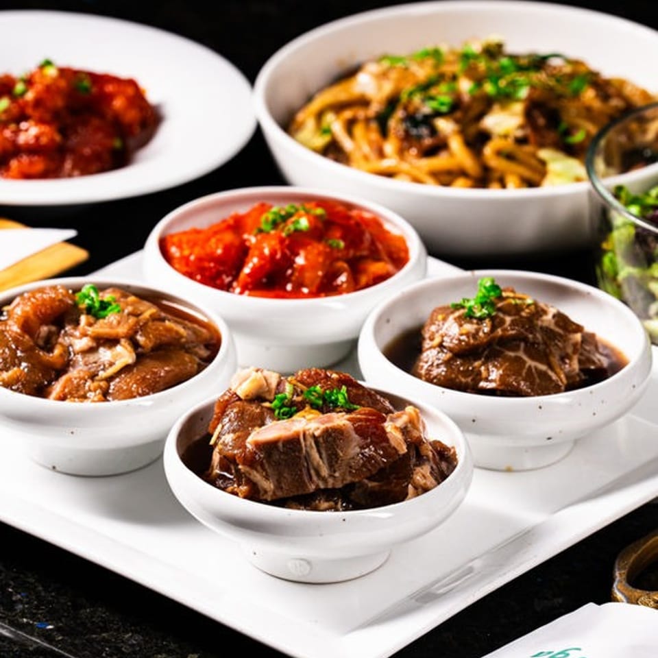 Assorted Asian dishes, including braised meats, noodles, and spicy red chicken, served in white bowls on a tray.
